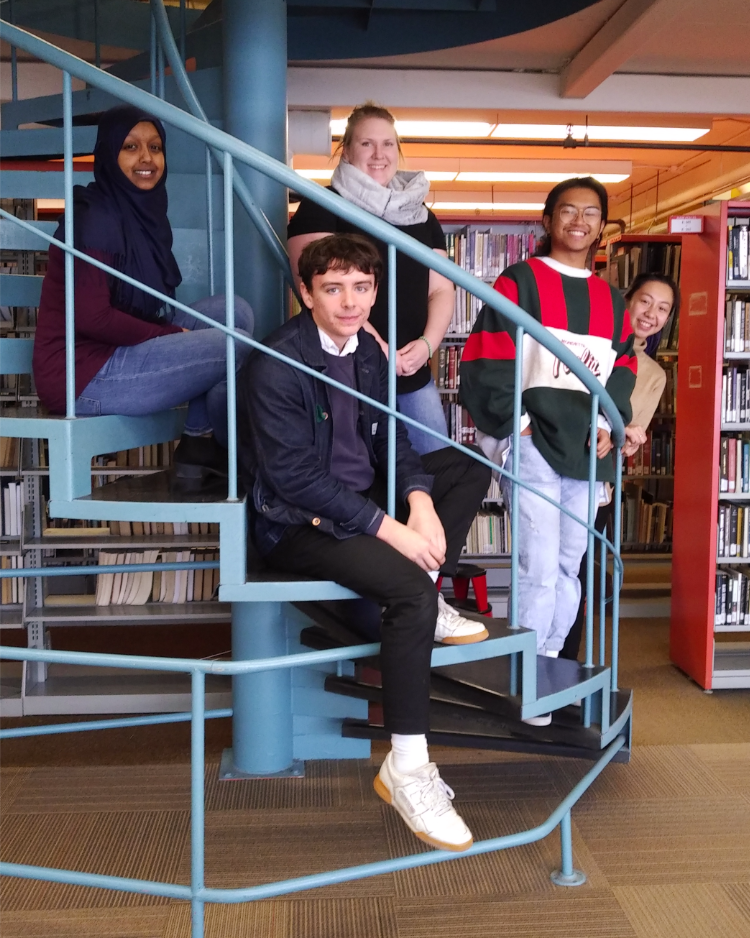 The UWinnipeg Library student assistants sit on a spiral staircase.