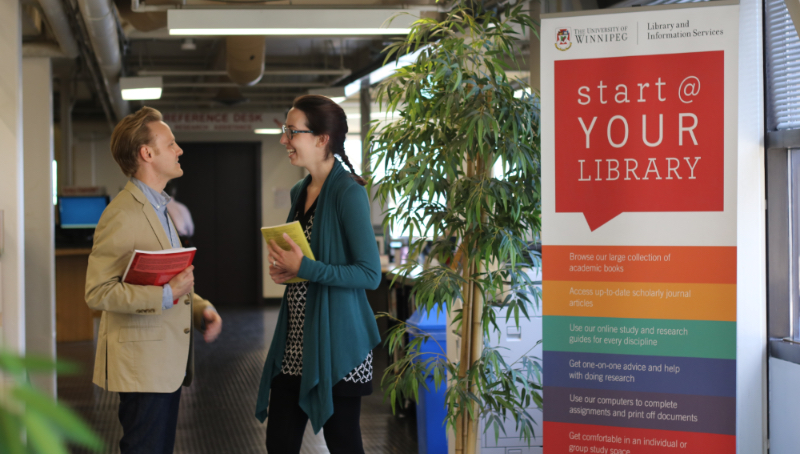 Faculty members meeting at the library entry with books in hand near a sign that says, "Start at Your Library."
