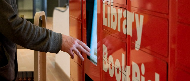 A hand reaching toward the book locker touchscreen.